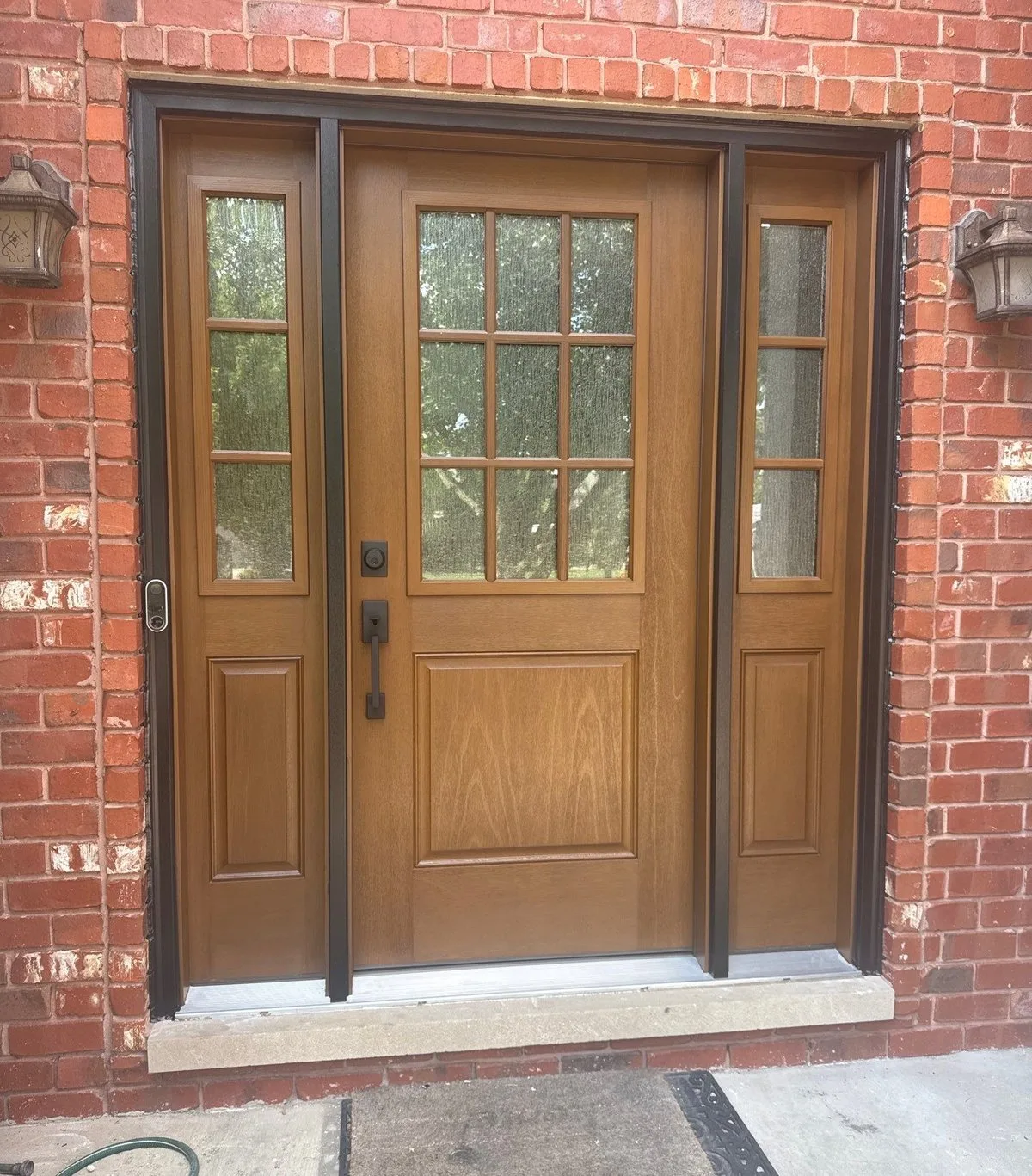 Fiberglass wood-tone front entry door with sidelights and divided-light upper panel installed by Americanstruction on an Orland Park home